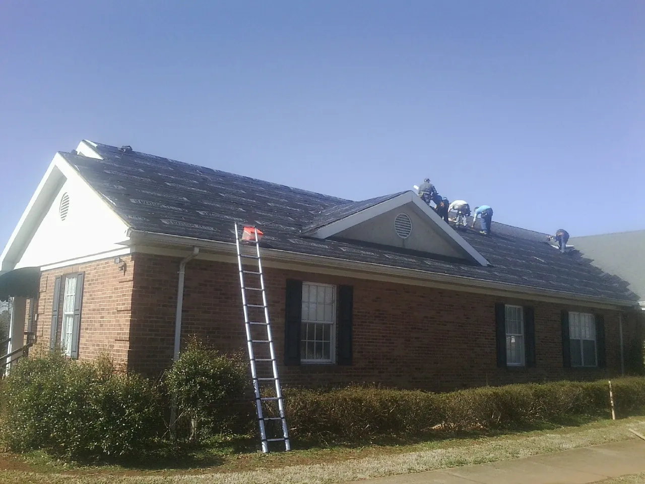Crew tearing shingles off a brick ranch roof with a ladder set — Metal Roof Repair work by our crew in Mount Holly Springs