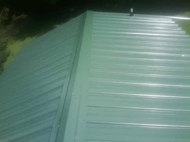 New green metal panels meeting at the ridge of a roof — Flat Roof Repair work by our crew in Mount Holly Springs