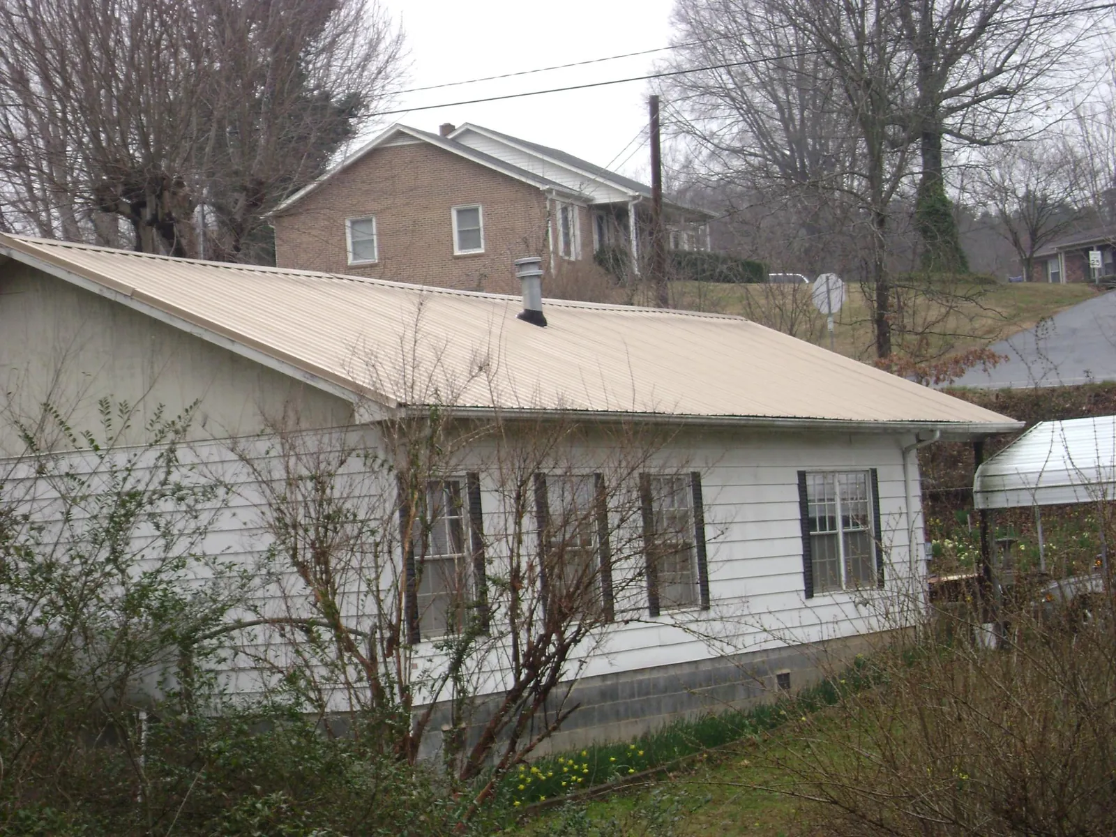 Tan metal roof on a white sided house set into a hillside — Commercial Roofing by Roofing Brothers in Mount Holly Springs